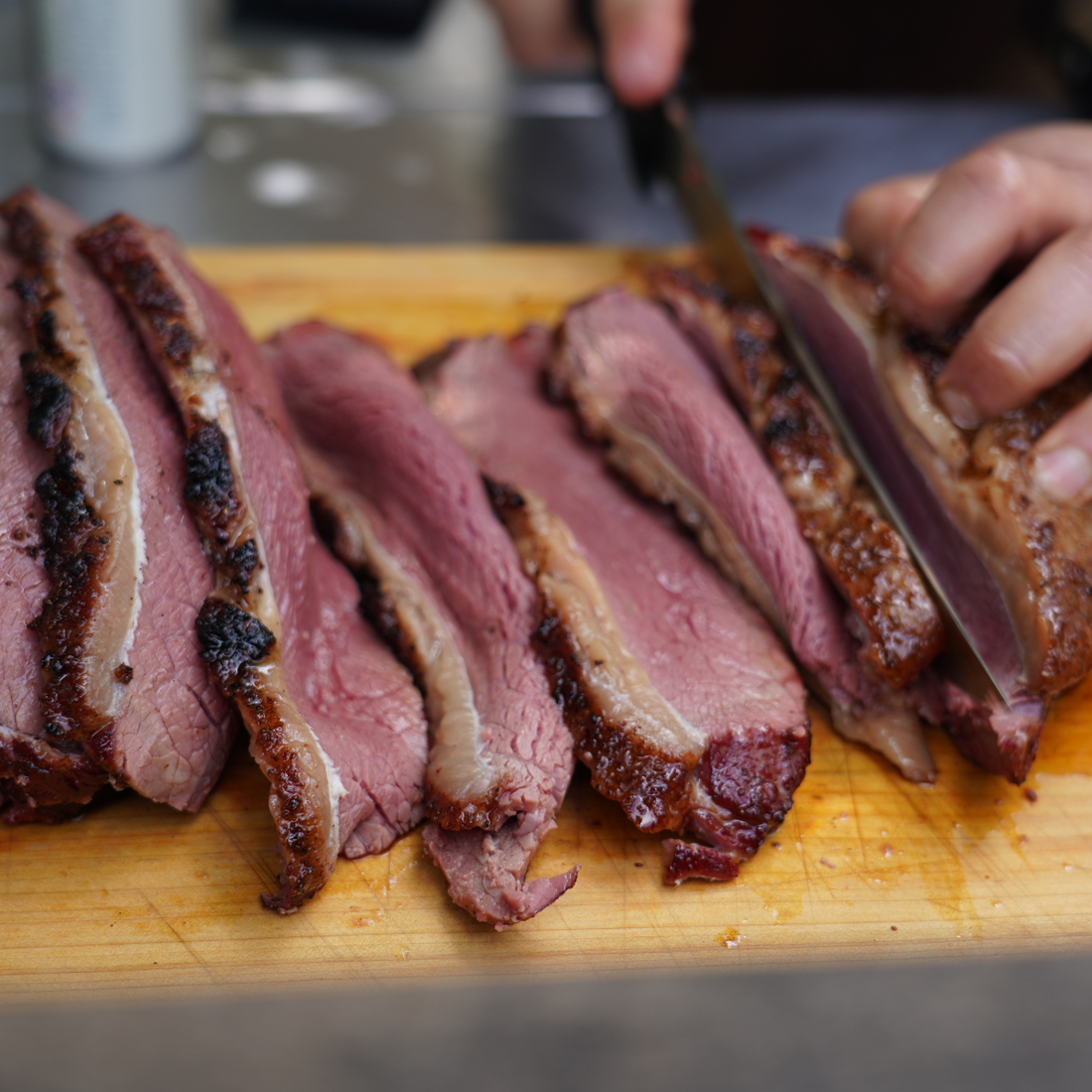 brisket being sliced on a wood cutting board to show how long to let brisket rest