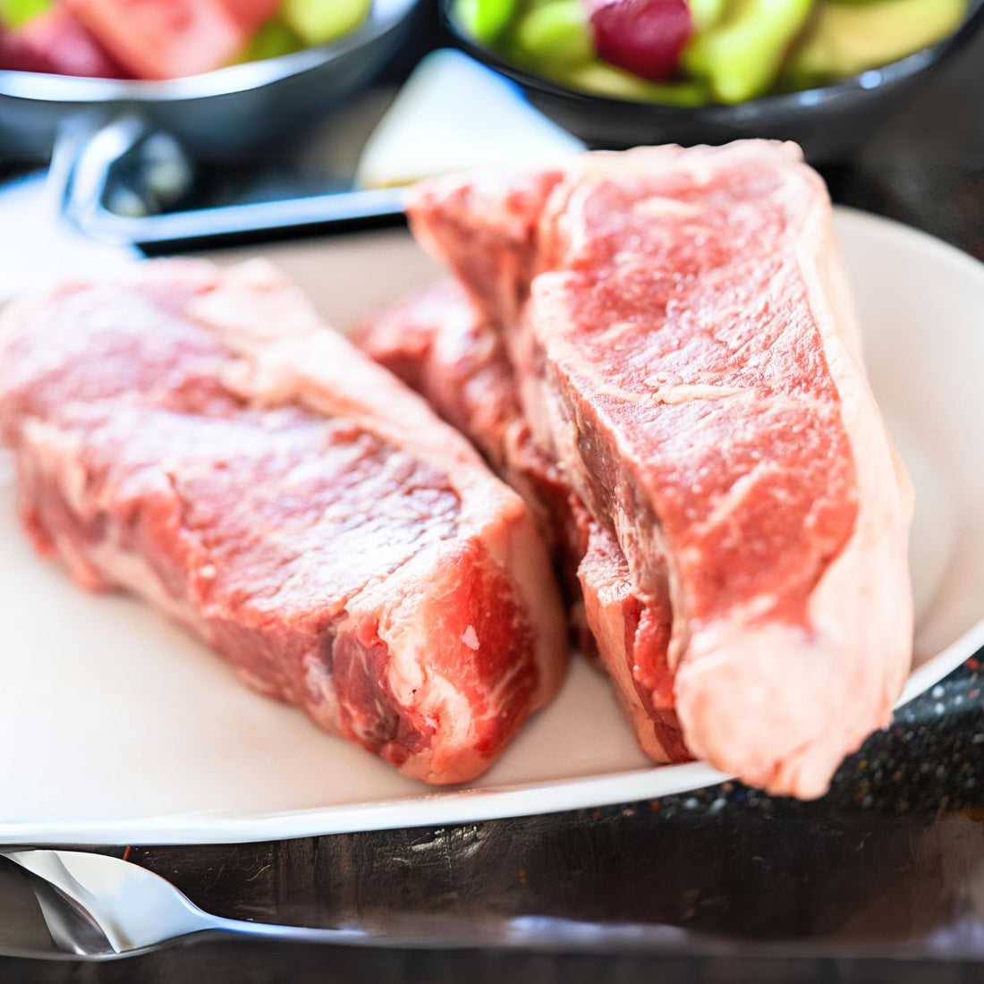 Two raw New York strip cuts over a white plate