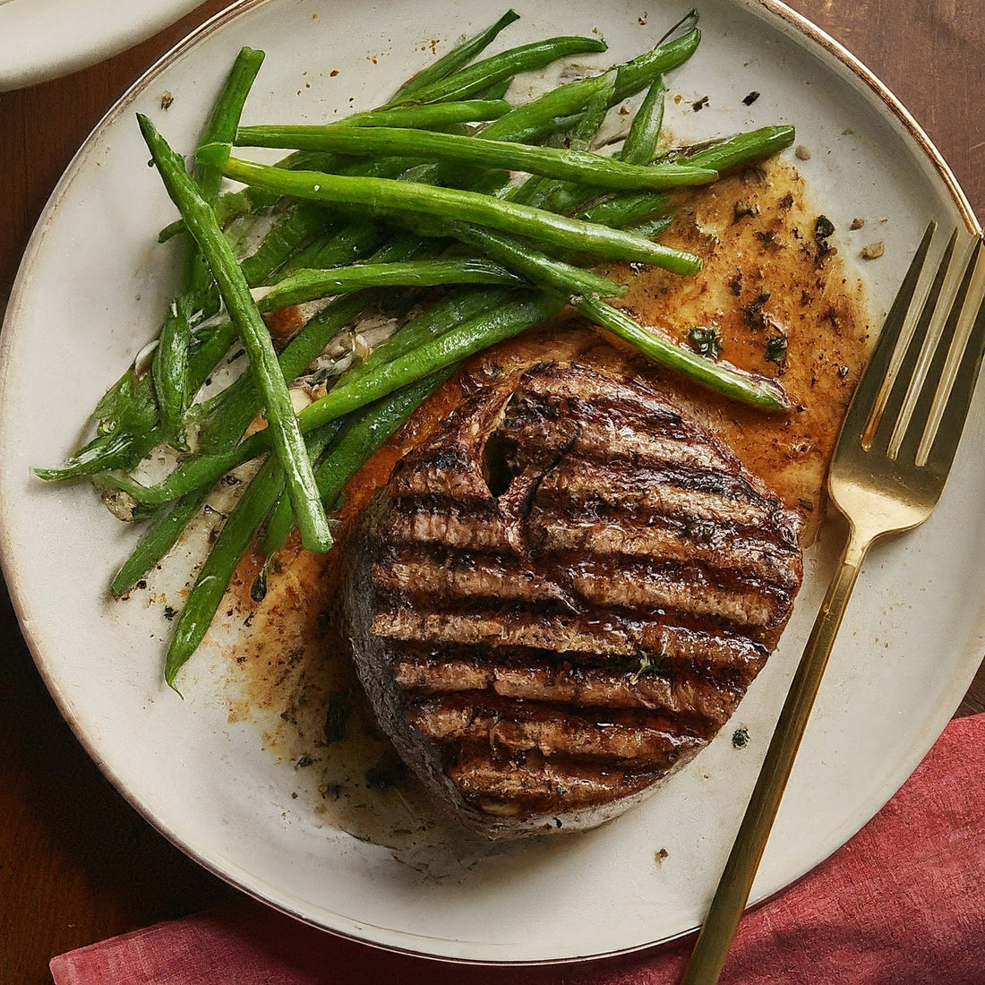 Juicy filet mignon with green beans and a fork over a round plate