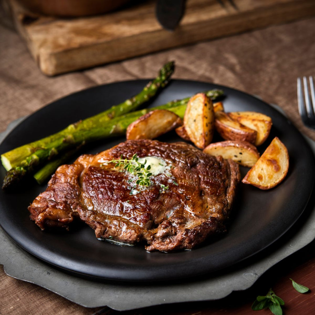 seared ribeye topped with butter, over a plate of roasted asparagus and potatoes