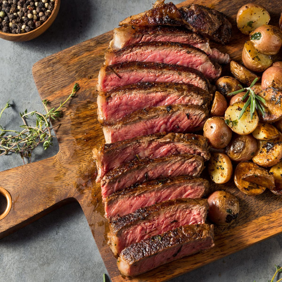 Sliced strip steak with potatoes over a wood cutting board
